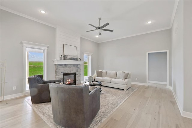 living area featuring ornamental molding, baseboards, a stone fireplace, and light wood finished floors