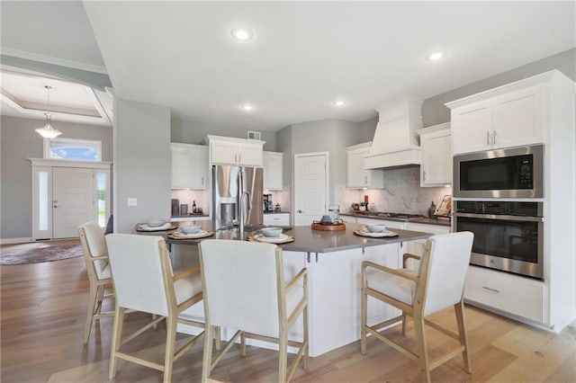 kitchen featuring stainless steel appliances, light wood-style floors, white cabinets, dark countertops, and a kitchen bar