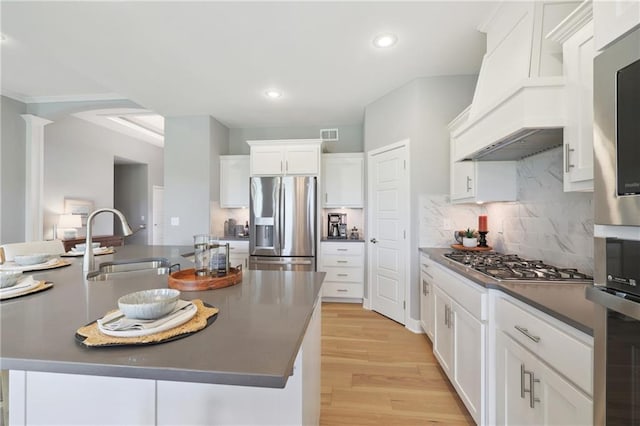 kitchen with stainless steel appliances, dark countertops, a kitchen island with sink, a sink, and white cabinetry