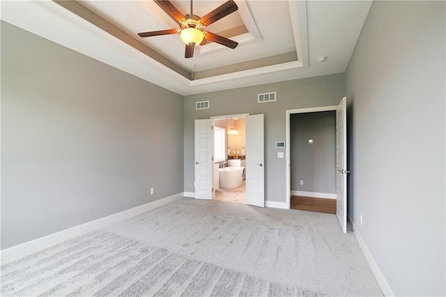 unfurnished bedroom featuring light colored carpet, a raised ceiling, visible vents, and baseboards