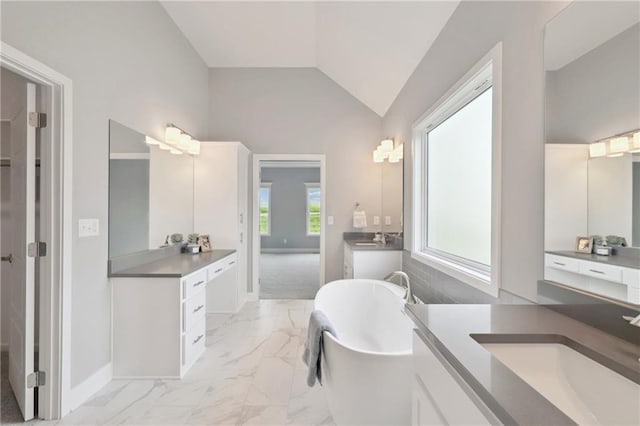 full bath with two vanities, a sink, vaulted ceiling, marble finish floor, and a soaking tub