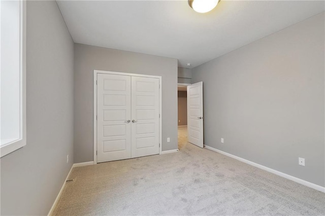 unfurnished bedroom with light carpet, a closet, and baseboards