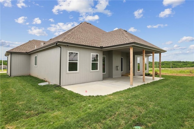 back of house featuring roof with shingles, a lawn, and a patio