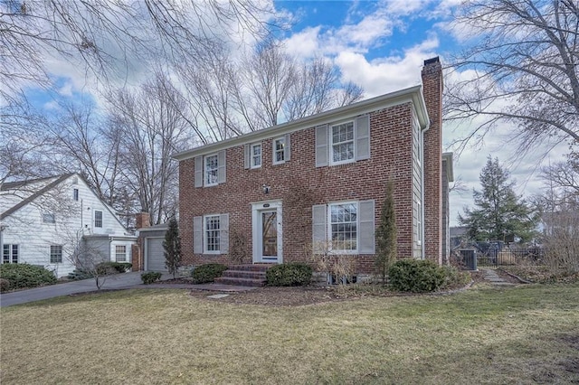 colonial-style house with driveway, a chimney, a front lawn, and brick siding