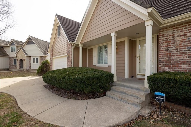 view of exterior entry featuring a garage, brick siding, and concrete driveway