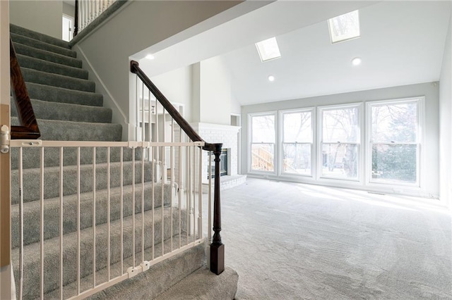 stairs featuring lofted ceiling with skylight, a brick fireplace, recessed lighting, and carpet