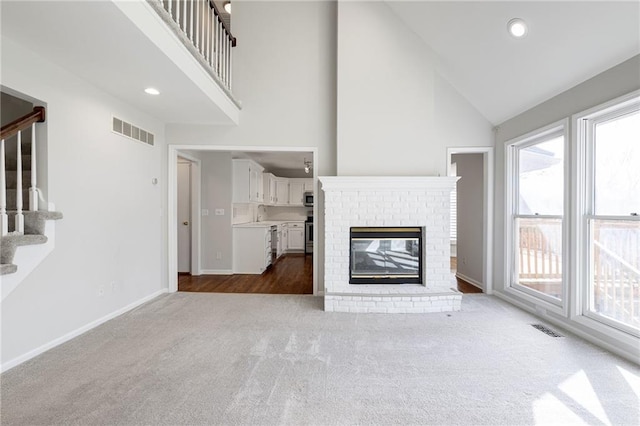 unfurnished living room featuring visible vents, high vaulted ceiling, stairs, and carpet floors