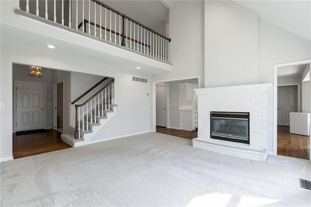 unfurnished living room featuring visible vents, an inviting chandelier, carpet flooring, a towering ceiling, and stairs