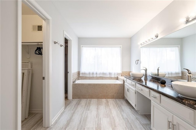 full bathroom featuring a sink, visible vents, a bath, and double vanity