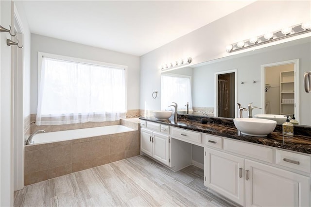 full bathroom featuring a sink, a spacious closet, a bath, and double vanity