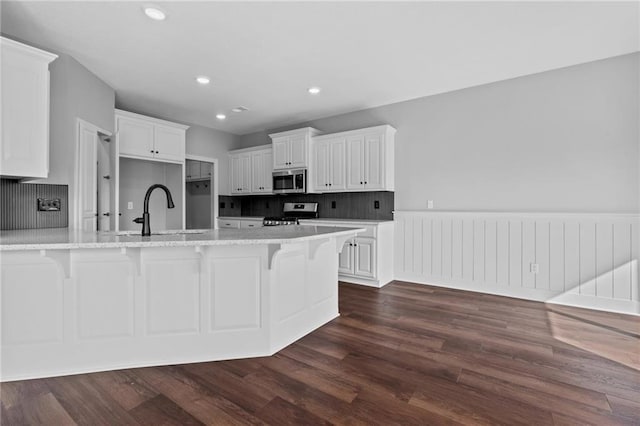 kitchen with appliances with stainless steel finishes, a sink, a kitchen bar, and dark wood-style floors