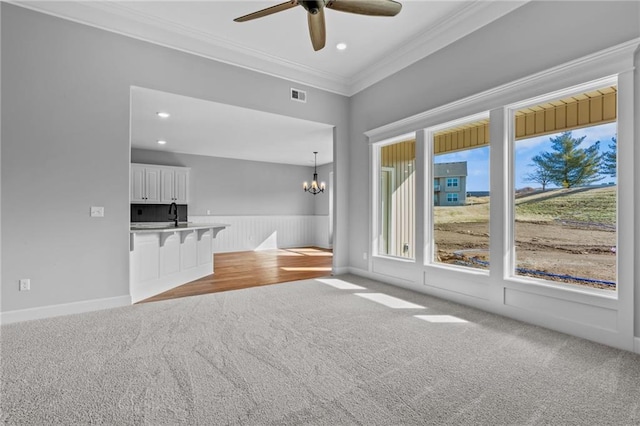 unfurnished living room with light carpet, recessed lighting, visible vents, ornamental molding, and ceiling fan with notable chandelier