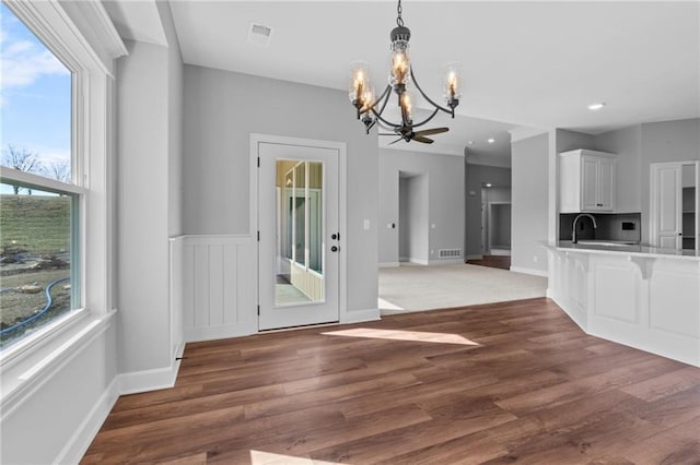 unfurnished dining area featuring a chandelier, visible vents, a sink, and wood finished floors