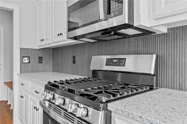 kitchen with stainless steel appliances, wood finished floors, light stone countertops, and white cabinets