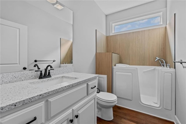 bathroom featuring toilet, a bathing tub, wood finished floors, and vanity