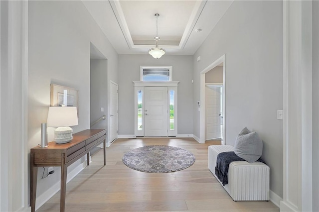 entryway with a raised ceiling, light wood finished floors, and baseboards