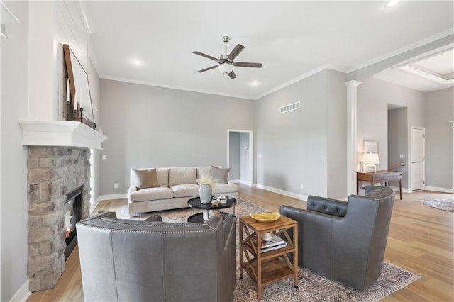 living area with light wood-type flooring, ceiling fan, a stone fireplace, and visible vents