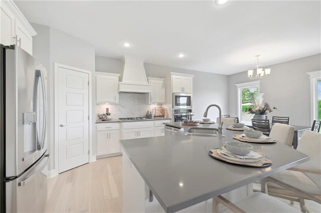 kitchen featuring a sink, premium range hood, a kitchen bar, a center island with sink, and stainless steel appliances