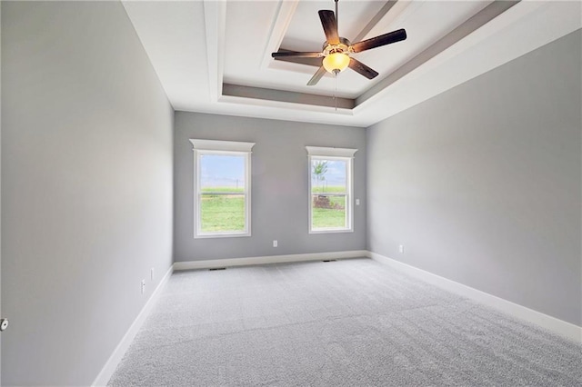 carpeted spare room featuring a tray ceiling, baseboards, and a ceiling fan