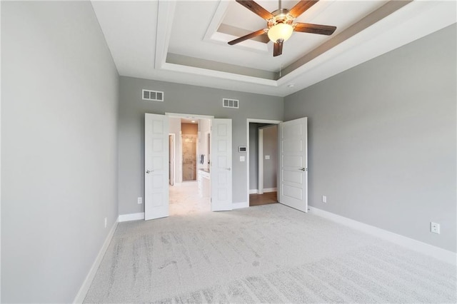 unfurnished bedroom featuring carpet flooring, visible vents, a tray ceiling, and baseboards