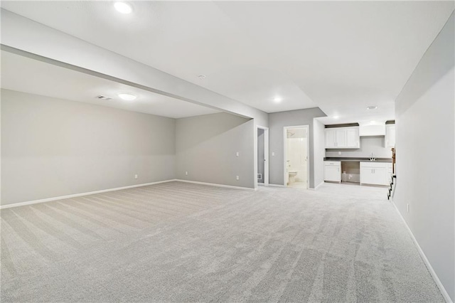 unfurnished living room featuring a sink, light colored carpet, baseboards, and recessed lighting
