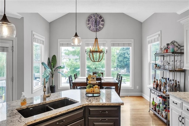 kitchen featuring hanging light fixtures, vaulted ceiling, light wood finished floors, and dark brown cabinets