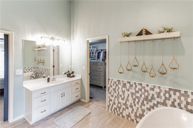 bathroom with a walk in closet, a freestanding bath, vanity, and wood finished floors