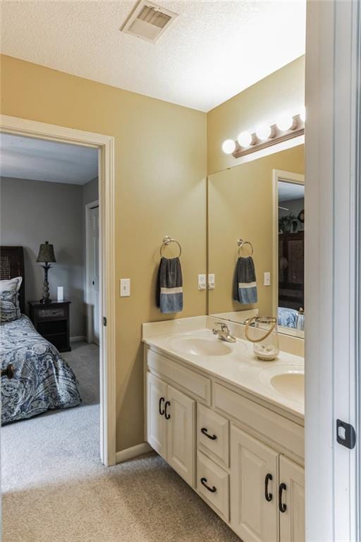 full bathroom featuring double vanity, visible vents, connected bathroom, a textured ceiling, and a sink