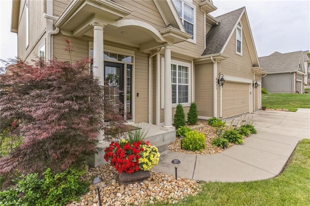 view of exterior entry with driveway, a shingled roof, and an attached garage