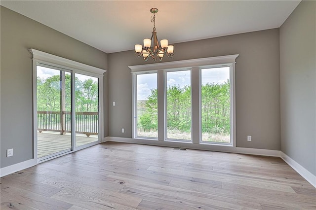 empty room featuring a chandelier, light wood finished floors, and baseboards