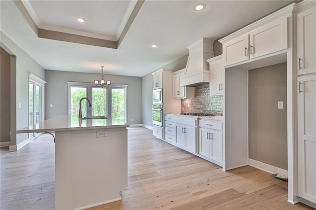 kitchen with a center island with sink, decorative backsplash, appliances with stainless steel finishes, light wood-style floors, and a sink