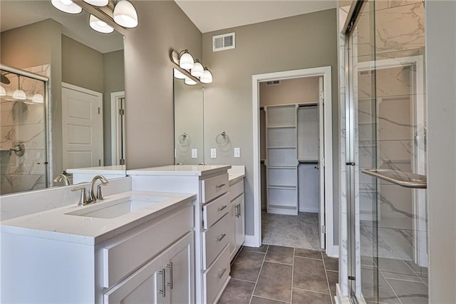 bathroom with a walk in closet, two vanities, visible vents, a stall shower, and a sink