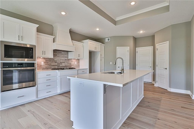 kitchen with light wood-style flooring, a sink, premium range hood, oven, and built in microwave