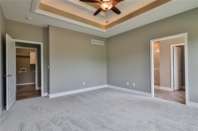 unfurnished bedroom featuring baseboards, carpet flooring, ensuite bathroom, visible vents, and a tray ceiling