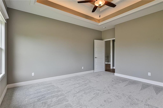 carpeted empty room with a tray ceiling, ceiling fan, and baseboards
