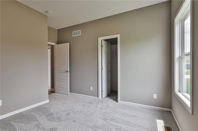 unfurnished bedroom with a walk in closet, baseboards, visible vents, and carpet floors