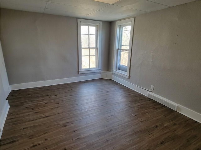 spare room with dark wood-type flooring, a drop ceiling, visible vents, and baseboards