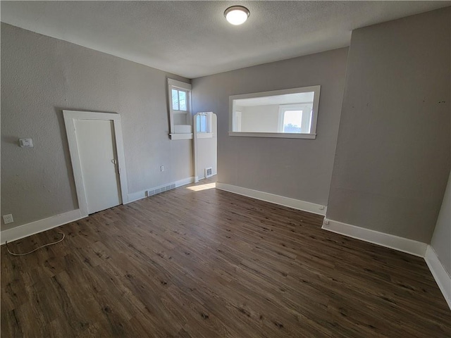 empty room featuring baseboards, a textured ceiling, visible vents, and dark wood-type flooring