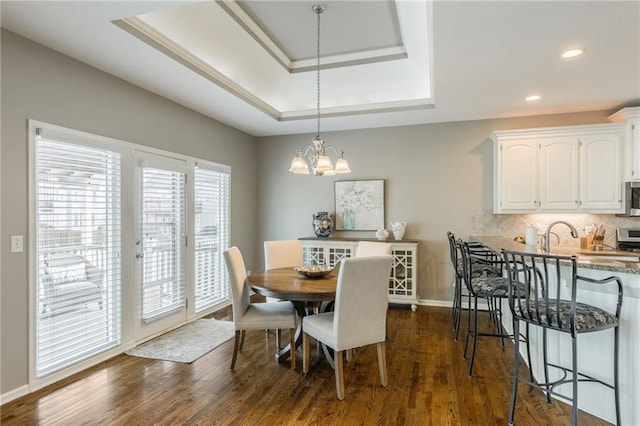 dining room with a raised ceiling, recessed lighting, baseboards, a chandelier, and dark wood-style flooring