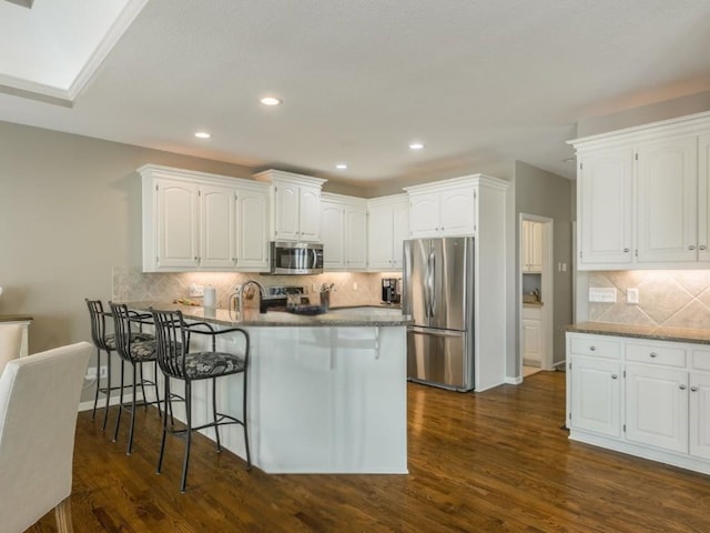 kitchen featuring stainless steel appliances, a kitchen bar, a peninsula, and white cabinetry