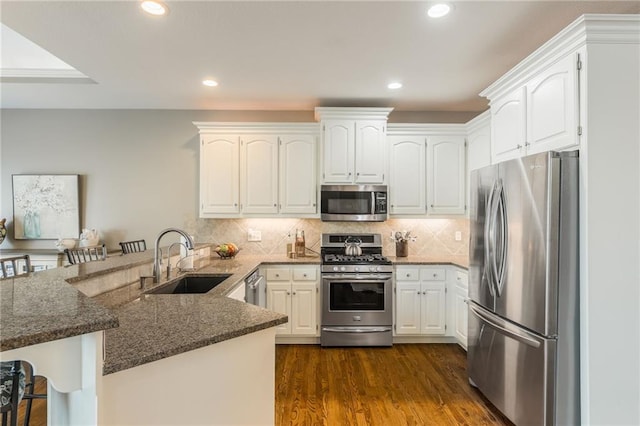 kitchen featuring dark wood finished floors, dark stone countertops, a peninsula, stainless steel appliances, and a sink