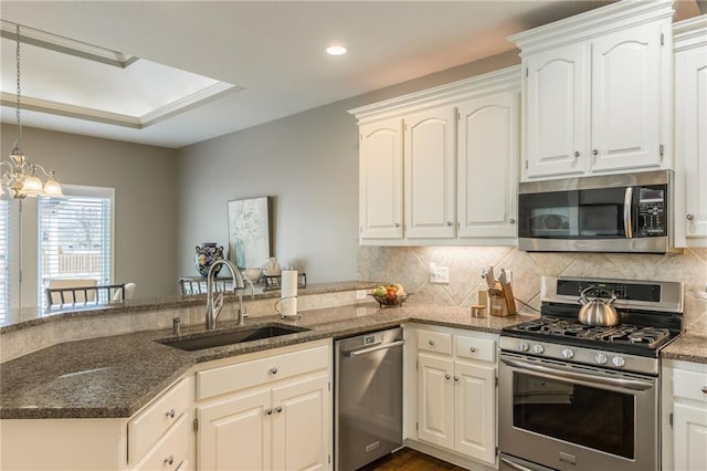 kitchen with a sink, dark stone countertops, tasteful backsplash, appliances with stainless steel finishes, and a peninsula