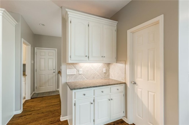 kitchen featuring backsplash, dark wood-style floors, dark stone counters, white cabinets, and baseboards