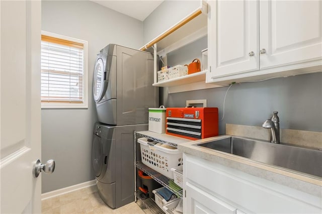 washroom featuring a sink, cabinet space, baseboards, and stacked washer and dryer