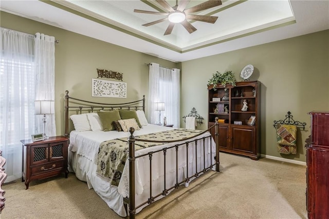 bedroom with baseboards, light colored carpet, a ceiling fan, and a tray ceiling