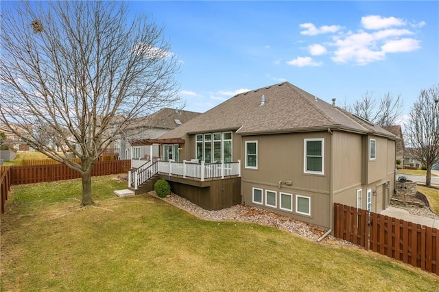 rear view of house featuring a wooden deck, a fenced backyard, a shingled roof, stairs, and a lawn