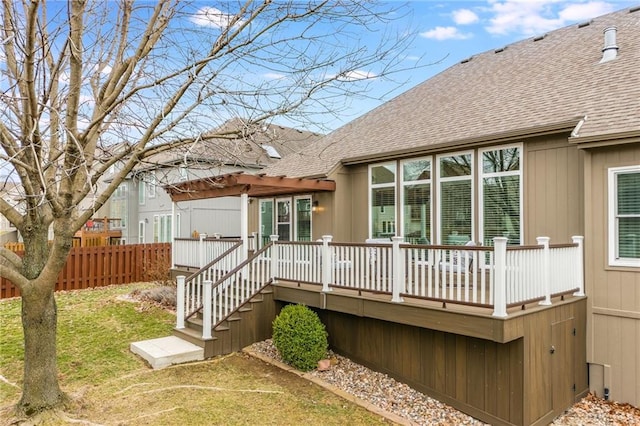 rear view of house with a shingled roof, fence, a wooden deck, a lawn, and a pergola