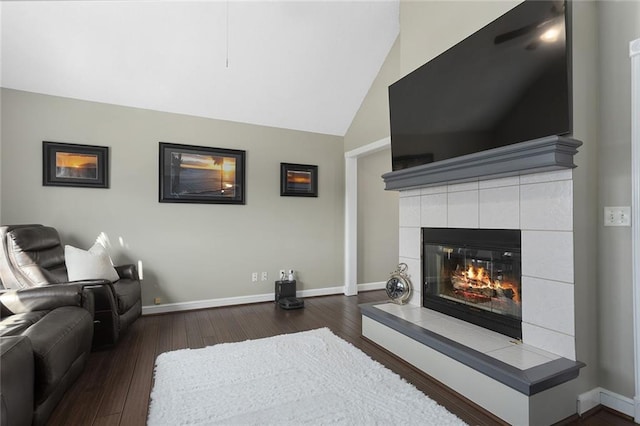 living room featuring a tile fireplace, dark wood-style flooring, lofted ceiling, and baseboards