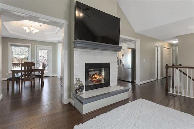 living area with baseboards, a raised ceiling, dark wood-style flooring, a fireplace, and a chandelier