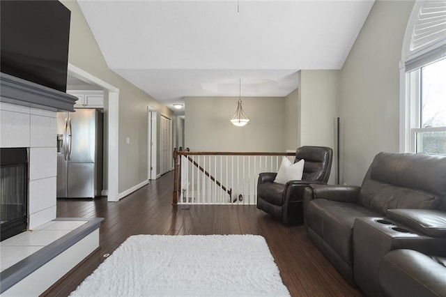 living area featuring dark wood-type flooring, baseboards, vaulted ceiling, and a tiled fireplace